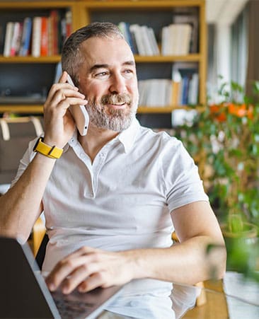 Businessman sitting at desk in bright office, talking on mobile phone